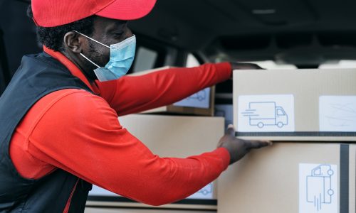 African delivery man loading boxes in the truck while wearing face mask to avoid corona virus spread