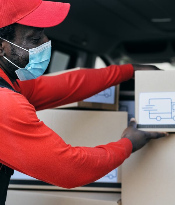 African delivery man loading boxes in the truck while wearing face mask to avoid corona virus spread